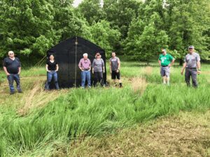 Group standing in grassy field by tent.
